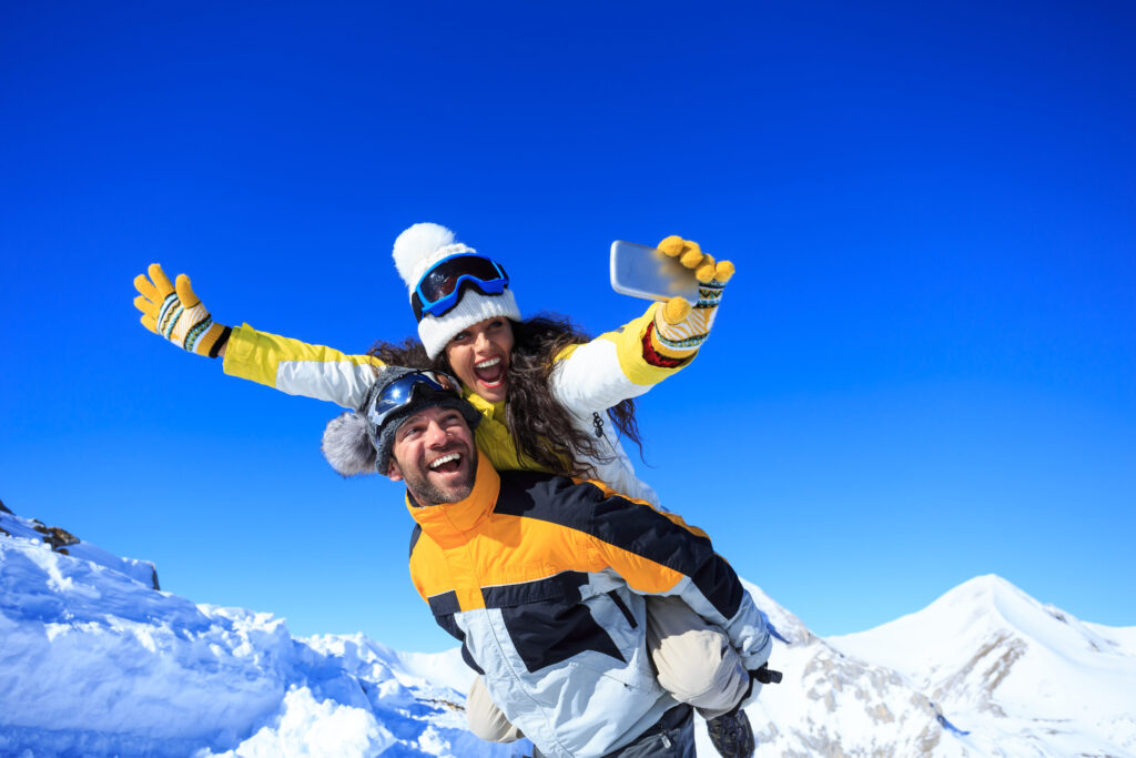 Cheerful young couple skiers having fun and making winter selfie